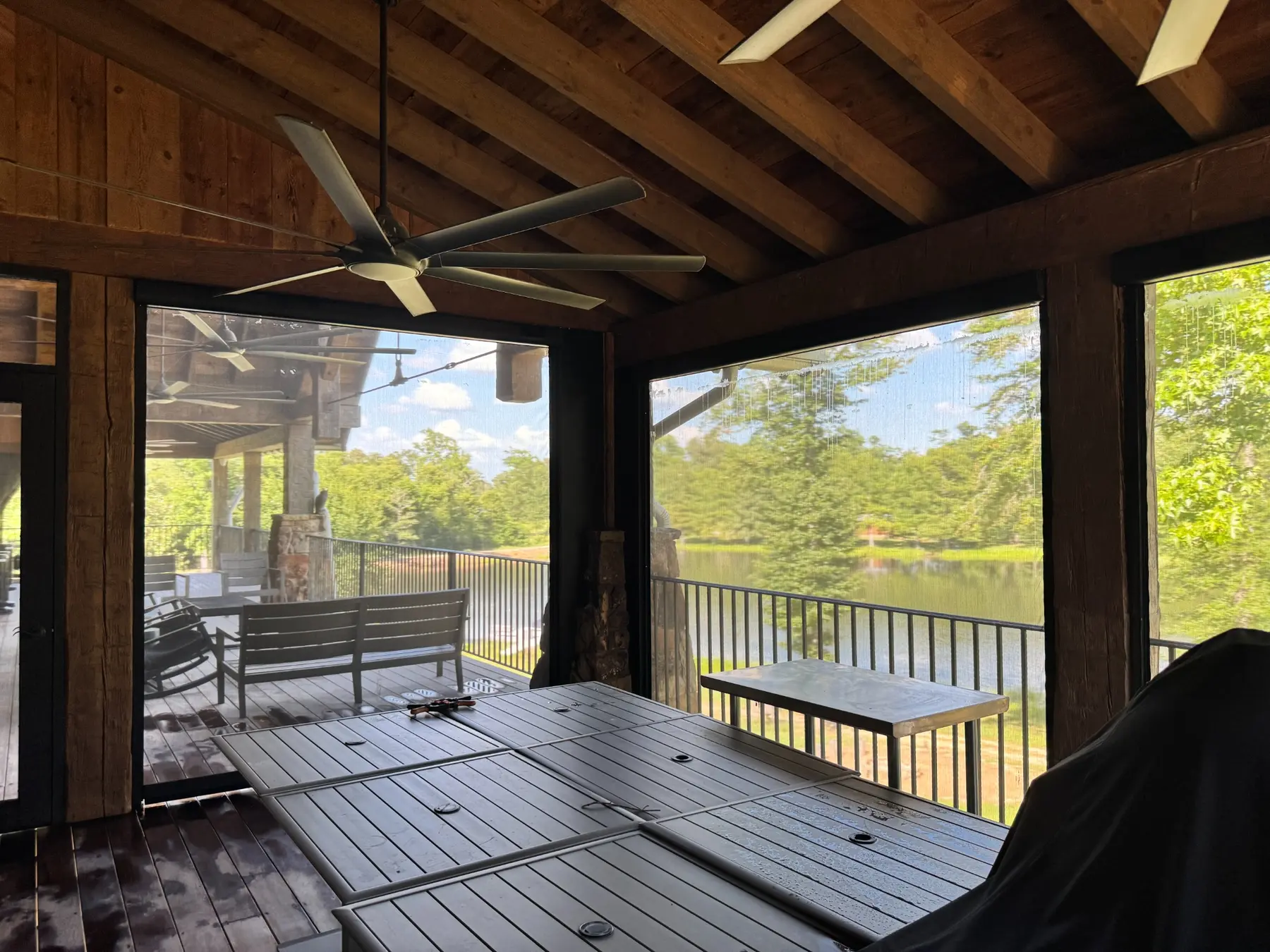 View through dark patio screen mesh toward a lake from a covered outdoor dining area.