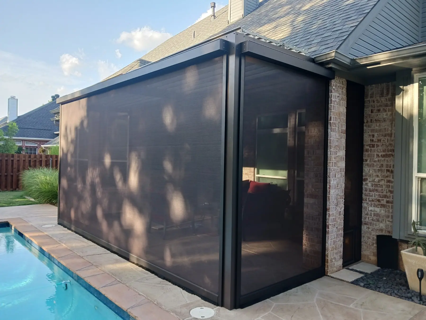 Dark motorized patio screens installed around a louvered roof beside a swimming pool.