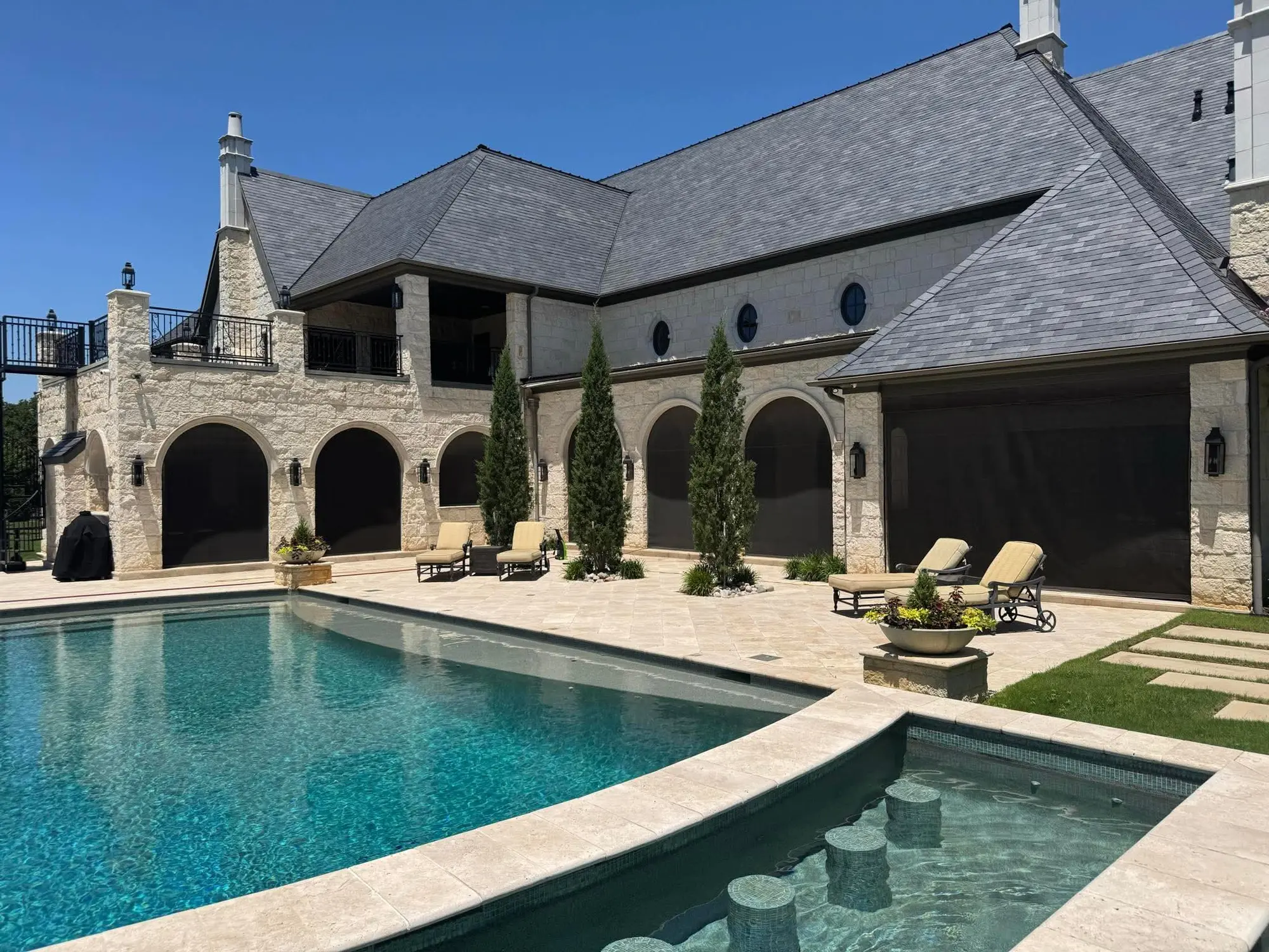 Large poolside residence with multiple dark motorized patio screens across arched and rectangular openings.