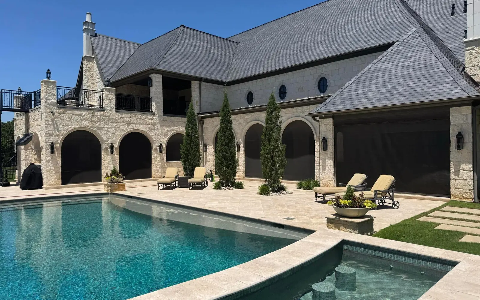 Large poolside residence with multiple dark motorized patio screens across arched openings.