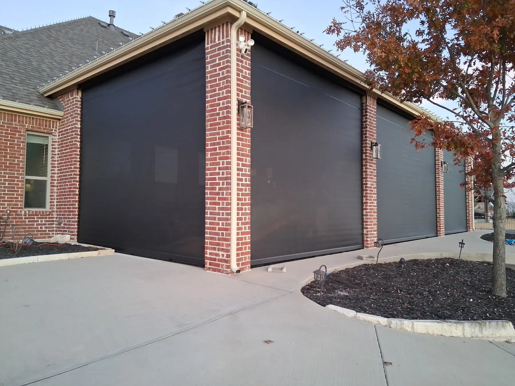 Three tall dark motorized patio screens installed between red-brick columns.
