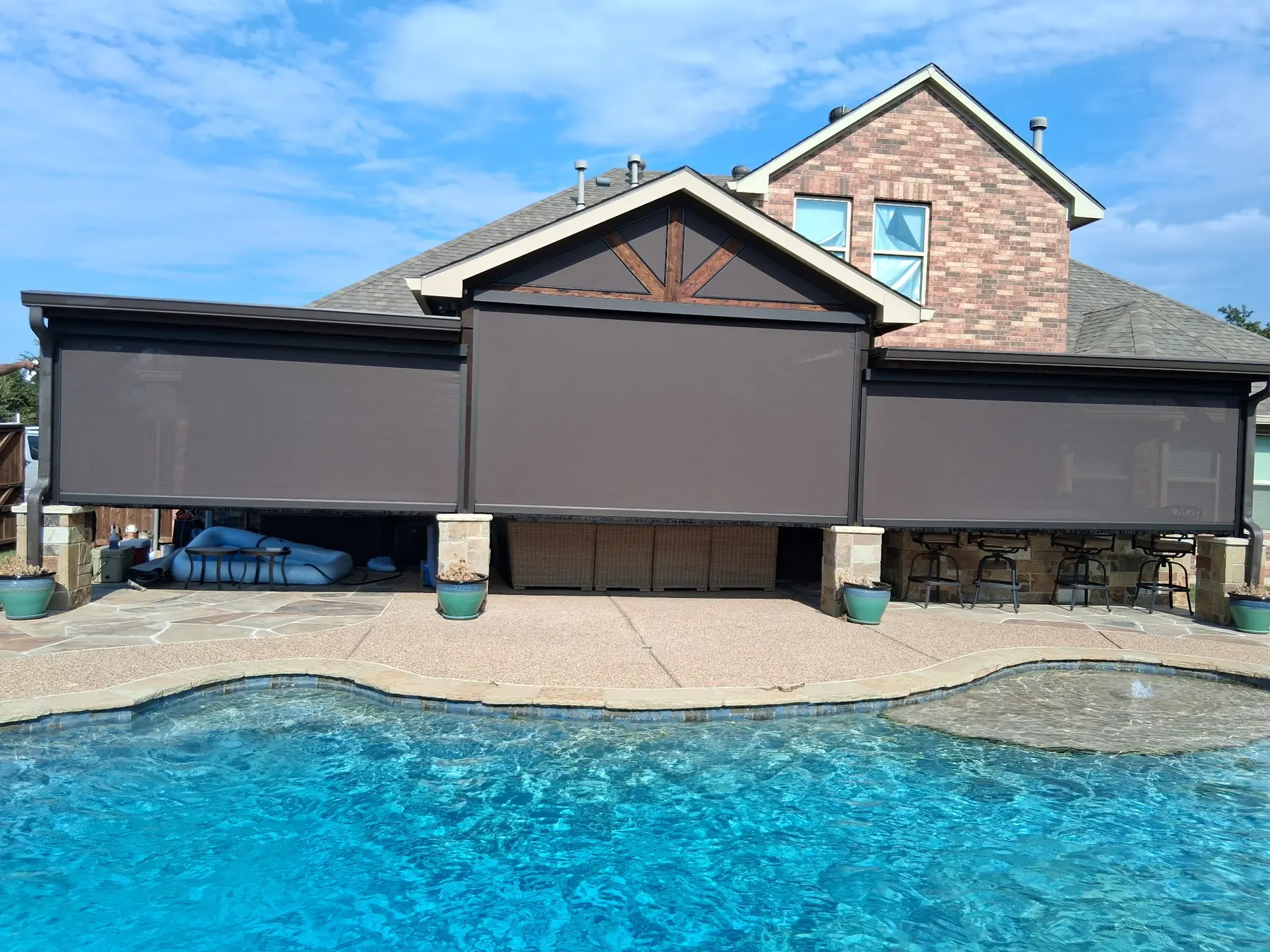 Three poolside motorized screens lowered to different heights across a covered patio.